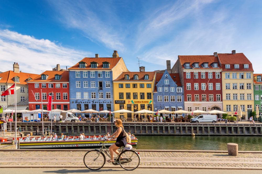 Copenhagen, Denmark - July, 2019: Copenhagen iconic view. Famous old Nyhavn port with colorful medieval houses, tourist ship and woman on a bicycle in the center of Copenhagen. Selective focus.